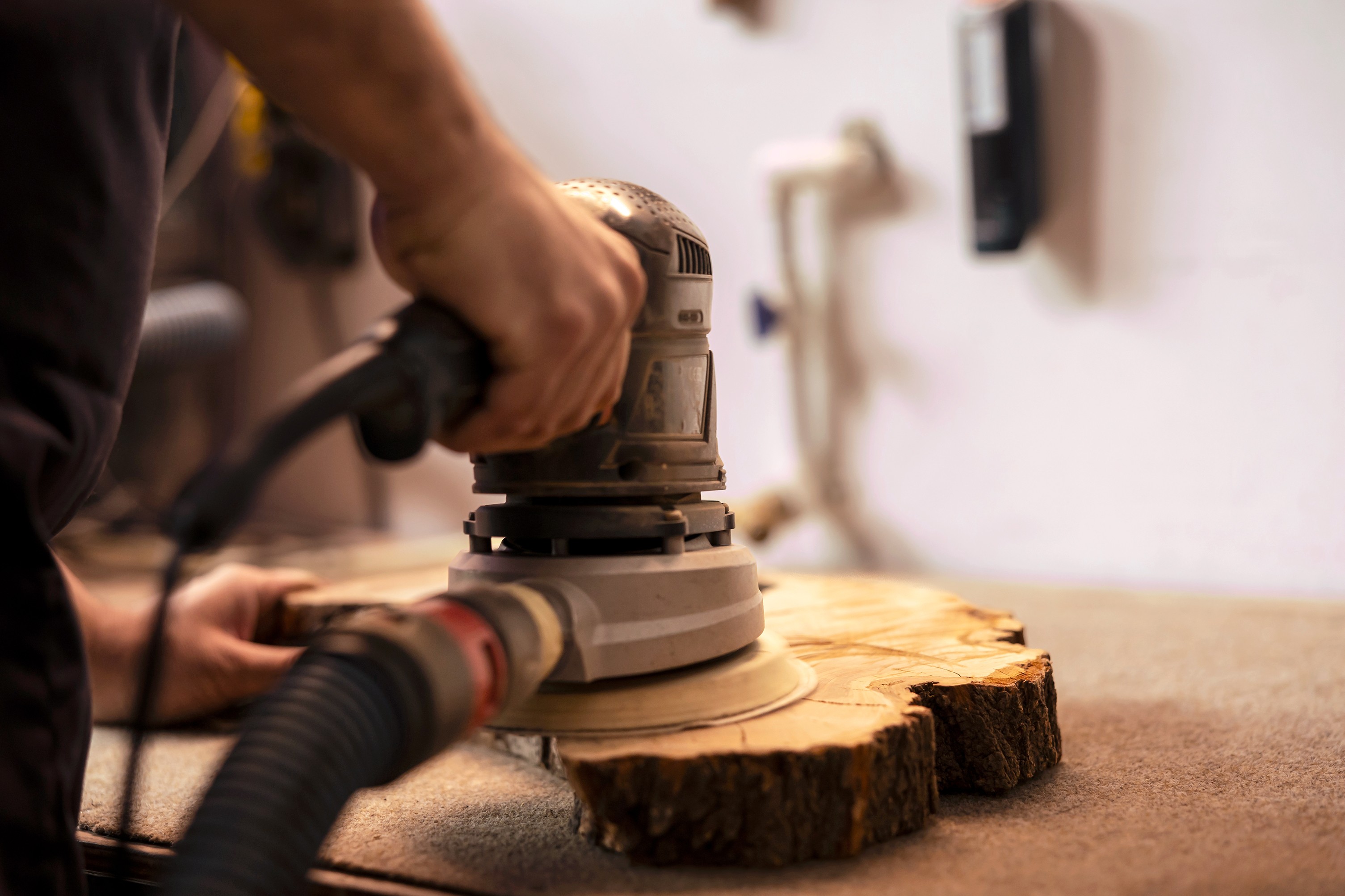Nahaufnahme einer Hand, die einen Exzenterschleifer auf einer Holzscheibe hält