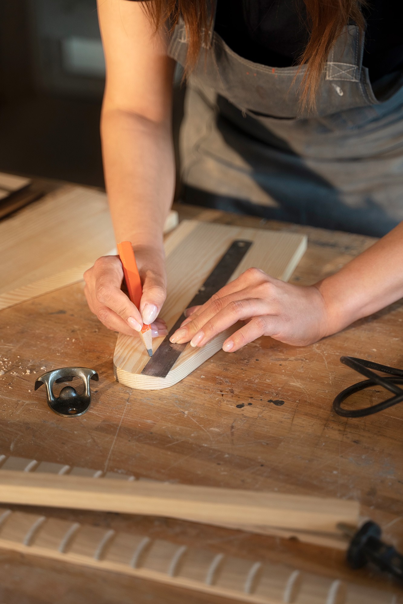 [DE] Frau zeichnet mit Bleistift und Lineal auf einem Holzstück in einer TischlereiWoman drawing on a piece of wood with pencil and ruler in a woodworking shop